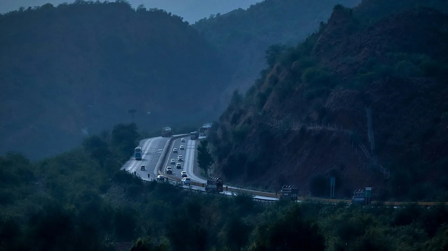 A motorway curving through green hills, with cars and trucks driving on it